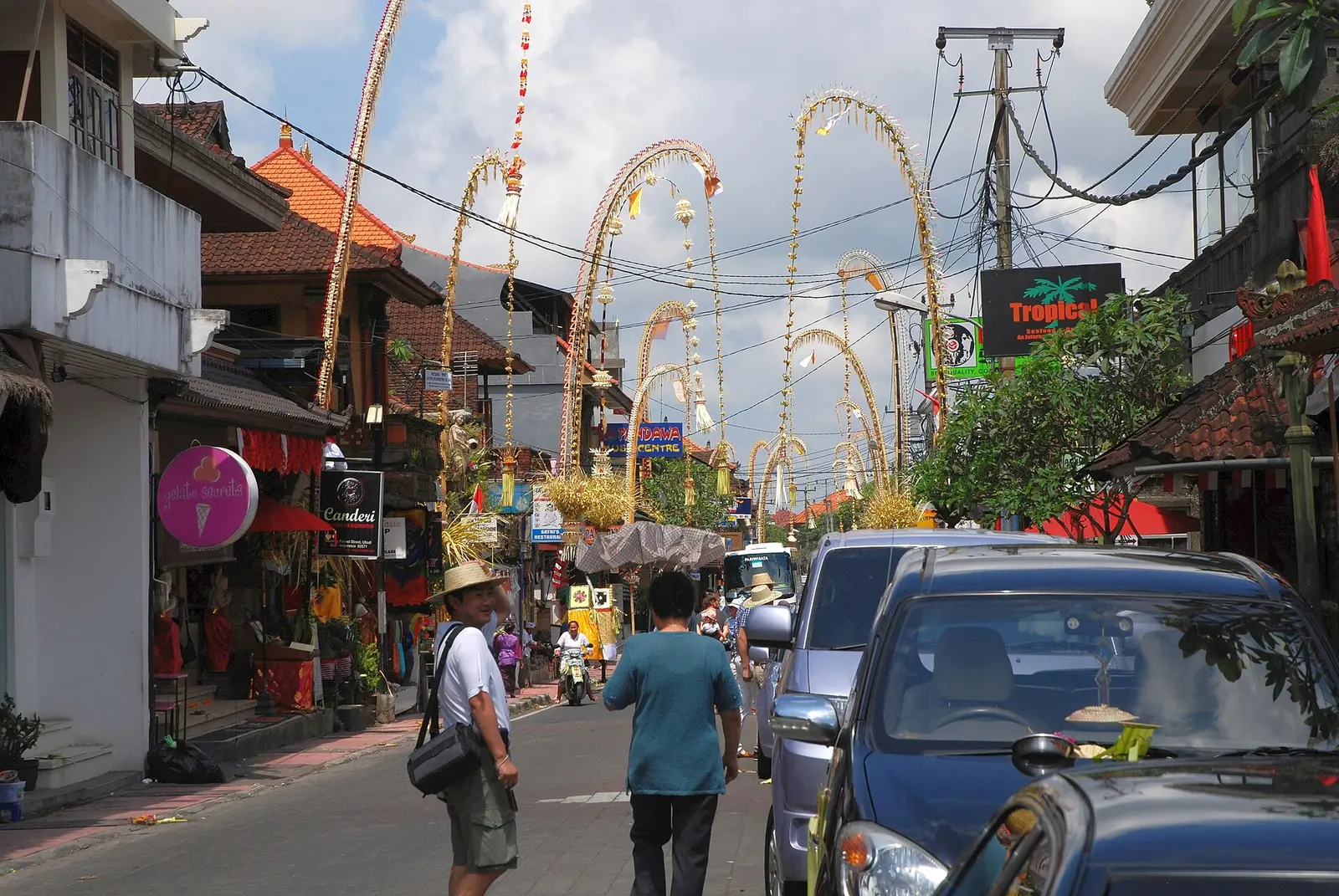 Tall decorated bamboo penjor arching over a street in Ubud during Galungan